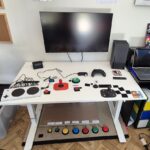 A variety of switches on a desk underneath a wall mounted monitor